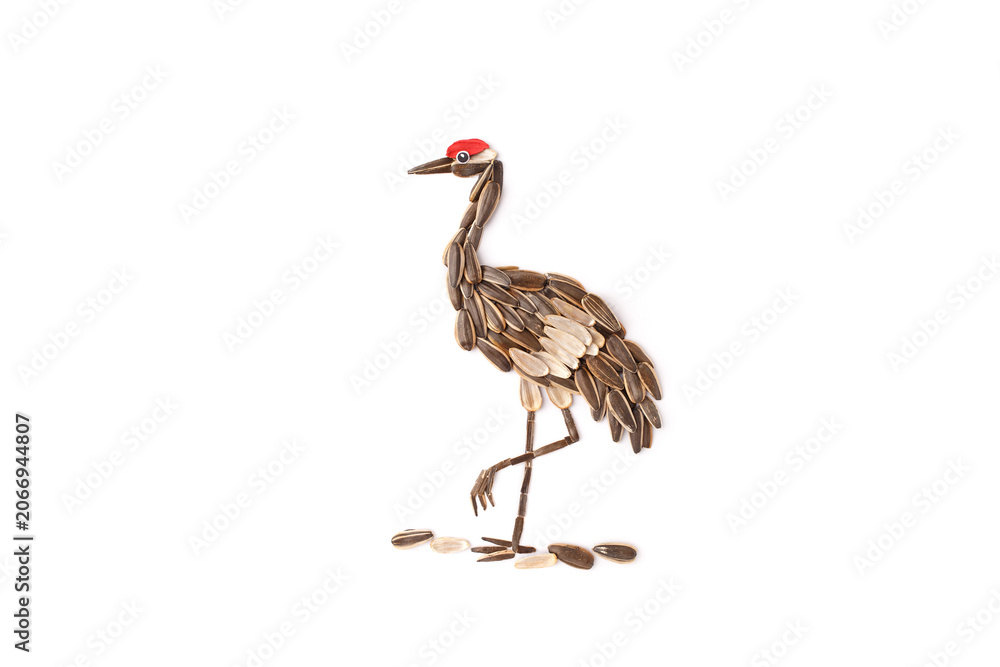 Obraz premium Crane bird made from sunflower seeds with red crown standing on white background. Seed art composition isolated on white background. Nature, wildlife and food creativity concept. Design for poster, 