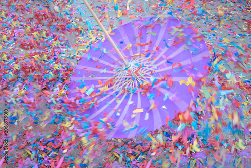 A purple umbrella spins through a sea of multicolored confetti, creating a dynamic blur that captures the energy and excitement of a festive event.