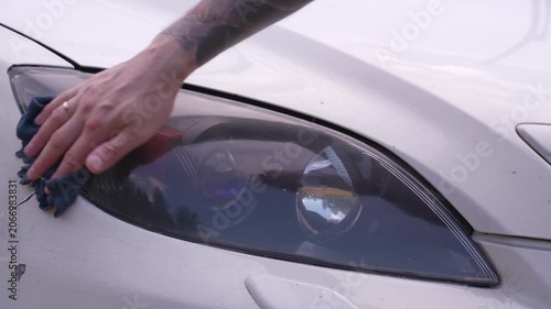 Wash the headlights of a car. A person washes the car's headlights with a sponge.