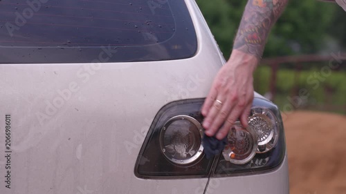 Wash the headlights of a car. A person washes the car's headlights with a sponge.