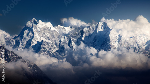 Dramatic Himalayan mountains landscape with snowy rocky peaks above clouds on sunny day, Nepal
