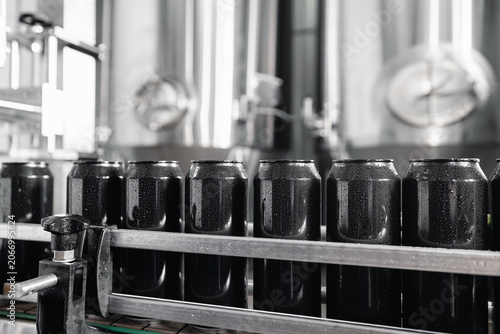 Obraz na plátně Rows of beer cans in modern brewery production line and stainless steel tanks
