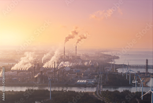 Obraz na plátne Industrial plant oil refinery releasing smoke near coastal wind turbines on sunr