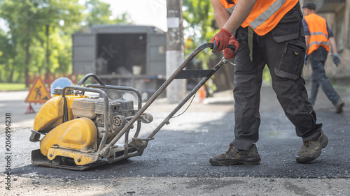Fotografía Road Worker in Orange Vest Pushing Yellow Vibratory Plate Compactor on Fresh Asp