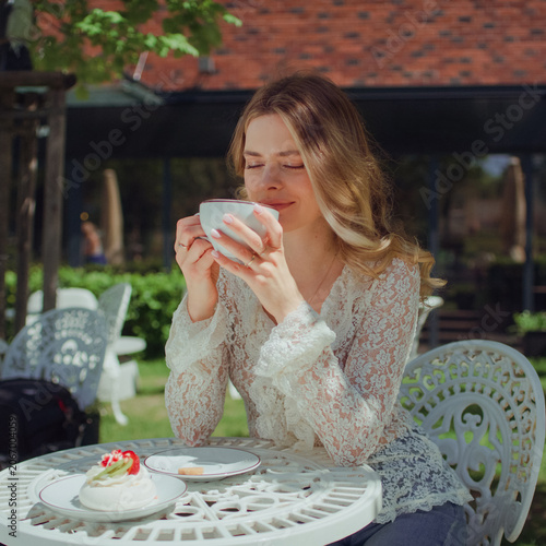 Confident woman sitting by a table at a park in an outdoor cafe and smelling a cup of cappuccino