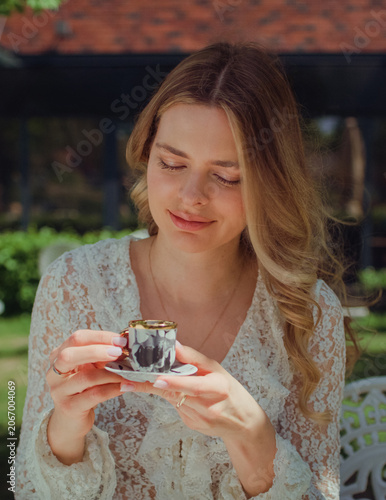 Woman sitting in an outdoor cafe and holding a tiny espresso cup. Smelling the coffee