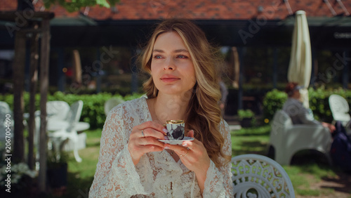Woman sitting in an outdoor cafe and holding a tiny espresso cup. Enjoying the warm weather