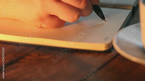 In the video, a woman's handwriting appears to write the word PLAN in a notebook lying on a wooden table next to a white coffee cup.