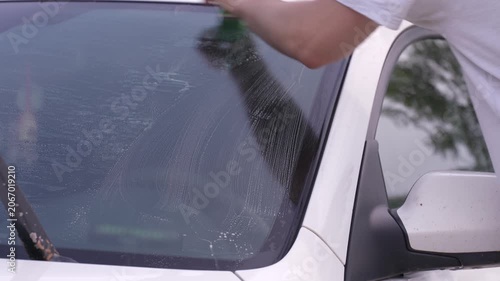 A man washes car windows with detergent before applying anti-rain