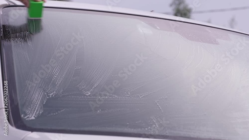 A man washes car windows with detergent before applying anti-rain