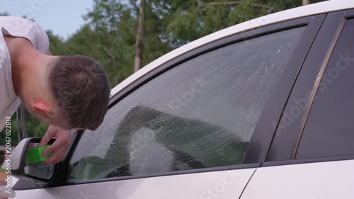 A man washes car windows with detergent before applying anti-rain