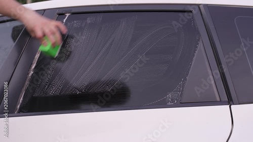 A man washes car windows with detergent before applying anti-rain