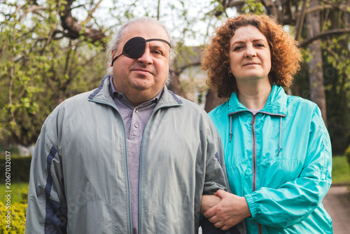 Bilde på lerret Middle-aged couple walking together with man wearing eye patch and supportive pa