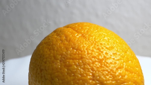 Close-up of a whole ripe orange rotating on a white turntable against a neutral background, highlighting its textured citrus peel under bright lighting.