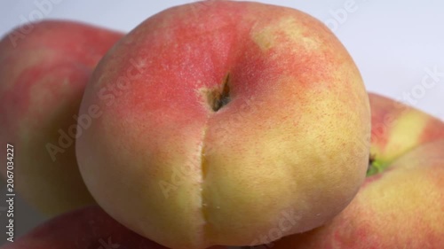 Close-up of a pile of flat donut peaches rotating on a white turntable, showcasing their unique shape and fuzzy skin under bright studio lighting.