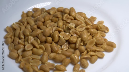 Close-up of roasted peeled peanuts rotating on a white plate, showcasing their smooth texture and golden color under bright studio lighting.