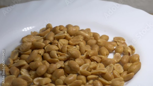 Close-up of roasted peeled peanuts rotating on a white plate, showcasing their smooth texture and golden color under bright studio lighting.