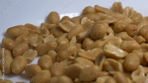 Close-up of roasted peeled peanuts rotating on a white plate, showcasing their smooth texture and golden color under bright studio lighting.