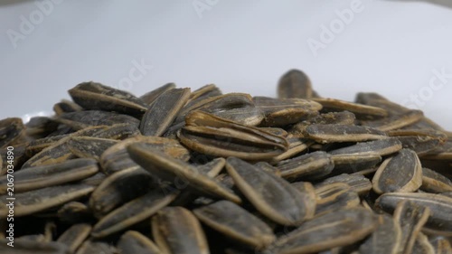 Close-up of a pile of roasted sunflower seeds in shells rotating on a white plate, highlighting their textured surface under bright studio lighting.