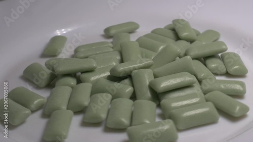 Close-up of a pile of green chewing gum pellets rotating on a white plate, showcasing their smooth glossy coating under bright studio lighting.
