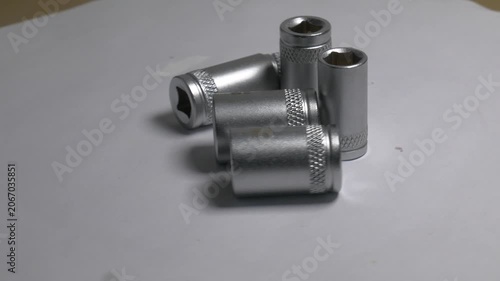 Close-up of metal socket wrench bits rotating on a white turntable, highlighting their metallic texture and knurled details under bright studio lighting.