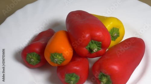Close-up of fresh red and yellow sweet bell peppers rotating on a white plate, showcasing their smooth texture and vibrant colors under bright studio lighting.