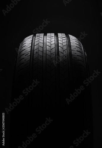 Car tire on dark background, front view. Moody automotive concept shot highlighting tire shape and texture.