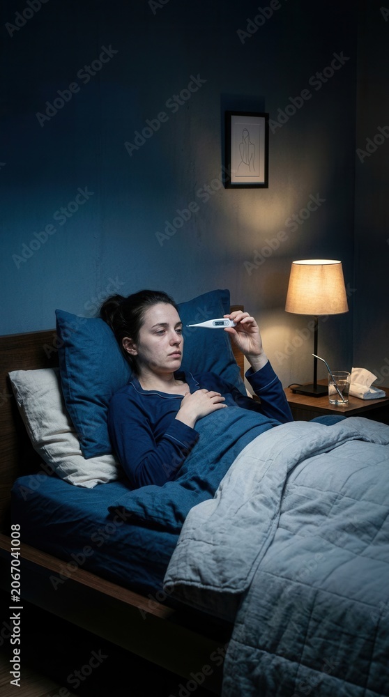 Fototapeta premium Woman Takes Temperature In Bed At Night Feeling Unwell Illness