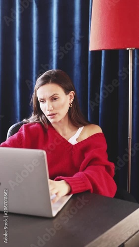 Confused Woman Frowning and Shrugging While Typing on Laptop, Looking at Screen with Perplexed and Shocked Expression, Sitting at Desk in Cozy Room with Blue Curtains and Red Lamp