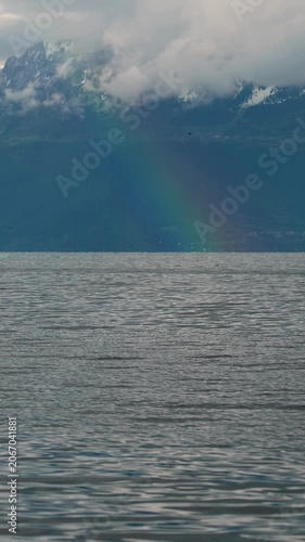 Real Time Rainbow over Lake Geneva and mountain in cloudy day. Preverenges, Vaud, Switzerland. Vertical
