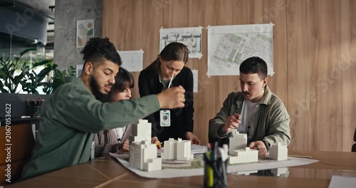 Five people discuss ideas and build a model in a design studio with plans on the walls