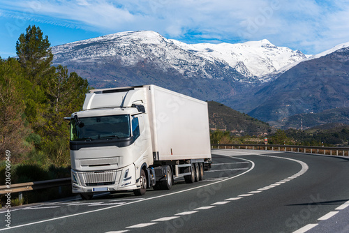 Refrigerated semi trailer truck driving on road with snow covered Sierra Nevada mountains in background