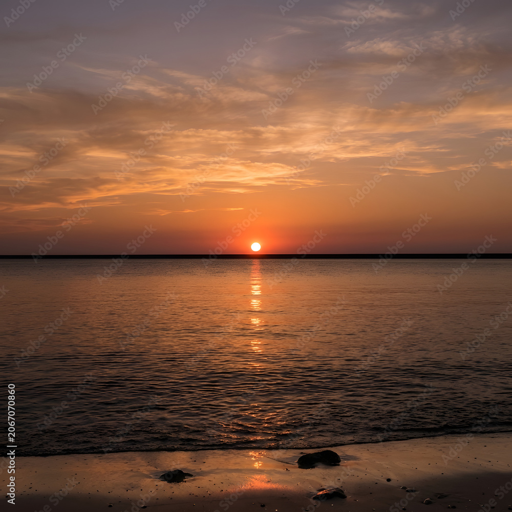 Fototapeta premium Sunset over calm water with distant city lights.
