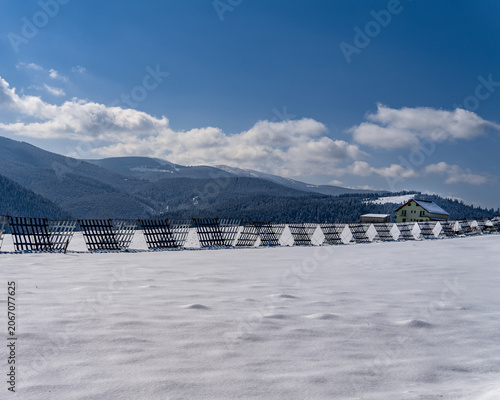 Wooden snow fence on a snowy plateau below forested mountains, Romania