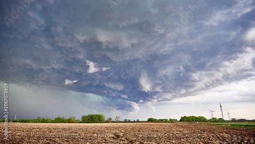 Tablou pe pânză Dramatic storm clouds hovering over a vast agricultural field with wind turbines