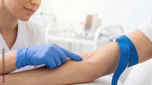 A medical staff member prepares to collect blood from a patient. The patient sits calmly while the staff member points at the area for the procedure
