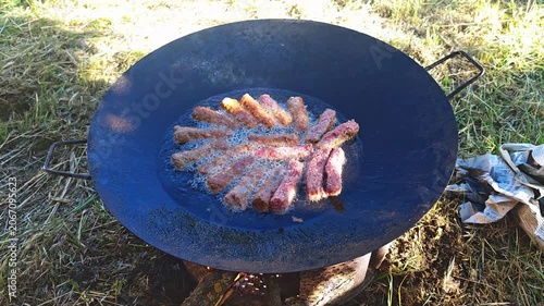 Sausages cooking in large frying pan over an open fire outdoors  