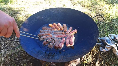Man grilling sausages in a wok over outdoor fire in nature  