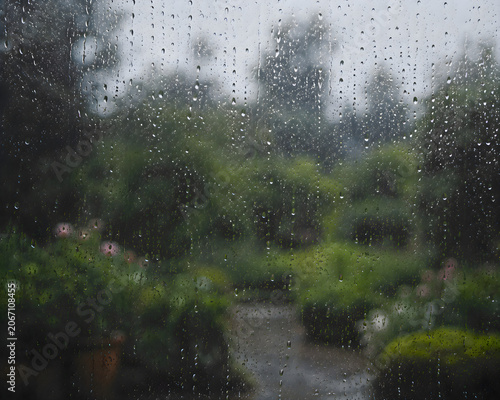 View of a garden through a rain soaked window, wet glass with water drops autumn storm seasonal atmospheric weather landscape portrait asset
