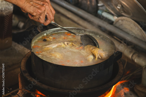 Fotografía Close up of a person stirring a big pot of hot boiling chicken rice porridge soup on a traditional wood stove