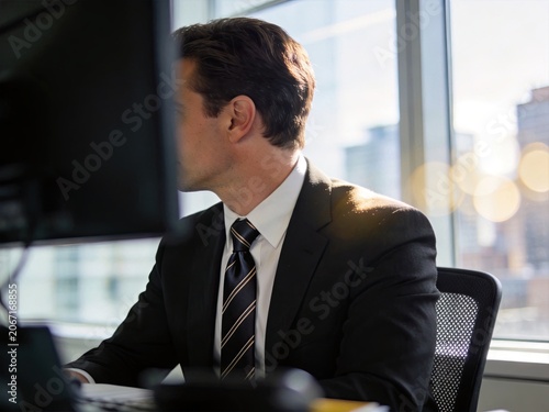 Professional man working at computer in modern office with city view through window, corporate executive, focused businessman, financial district background, career success