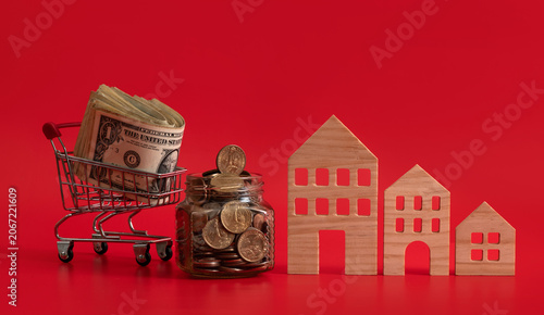 фотографія Glass jar with US coins and symbolic wooden houses on a red background