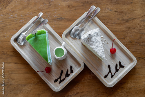 white snow cream coconut cake one piece and matcha pandan cake with green tea sauce cherry chocolate sauce and dual spoon in wooden tray table with empty sign tag in cafe bakery shop for sweet dessert