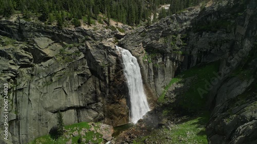 Aerial shot of Yosemite Valley featuring cascading waterfall surrounded by granite cliffs, dense forest, and dramatic mountain landscape in California’s Sierra Nevada.