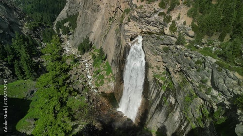 Aerial shot of Yosemite Valley featuring cascading waterfall surrounded by granite cliffs, dense forest, and dramatic mountain landscape in California’s Sierra Nevada.