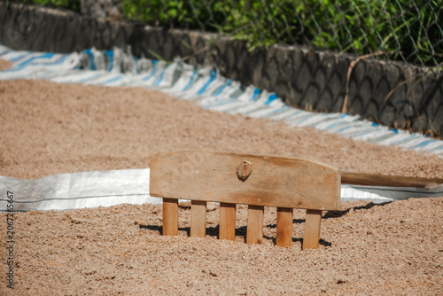 Closeup of a worker using a wooden rake to spread grains on a blue and white striped tarp
