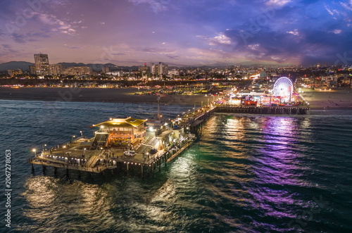 Santa Monica Pier at dusk glows as the Pacific sky shifts from gold to deep indigo, with the Ferris wheel lighting up against the fading horizon.