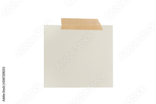 A blank square piece of white paper attached with a strip of beige masking tape, isolated against a solid black background, for copy space
