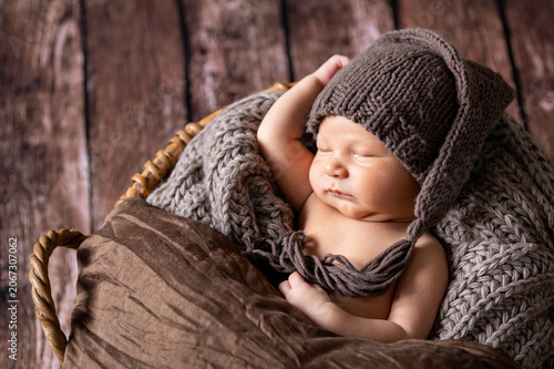 Sleeping newborn baby resting peacefully in a rustic basket, wrapped in a knitted blanket and wearing a soft, brown knitted hat on a wooden background