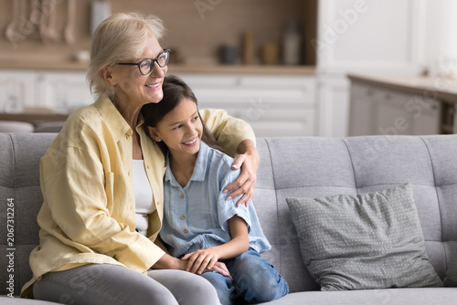 Bild auf Leinwand Loving older granny hugging her pretty little granddaughter seated on comfortabl